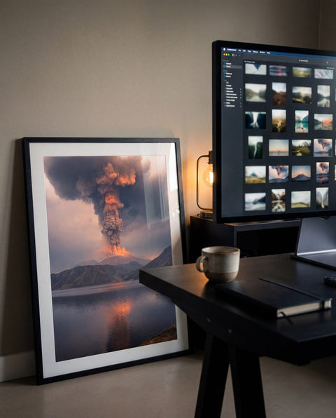 A framed generative fine-art print in a studio beside a monitor of image thumbnails, the curation moment behind chaipeau Artistic Intelligence.