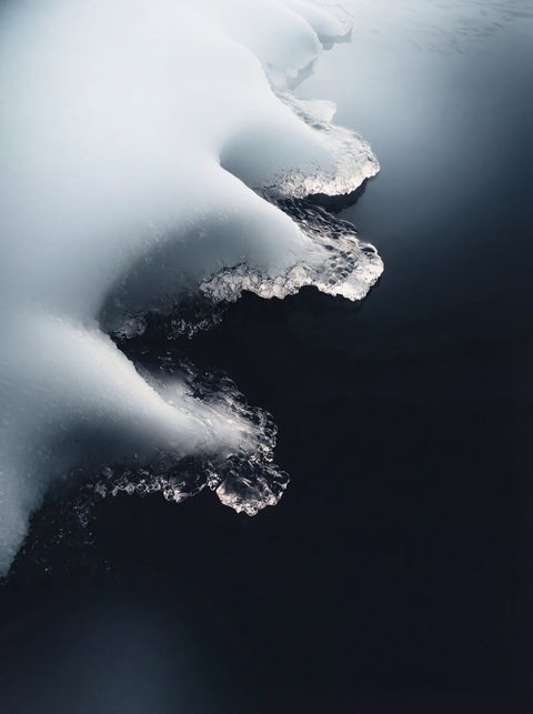 Generative art print of an aerial view of white sea ice meeting dark ocean water, high contrast abstract composition, framed in matte black solid wood.