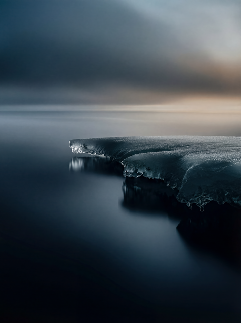 Generative art print of an ice shelf edge meeting calm water, long exposure effect, minimalist composition, framed in matte black solid wood.